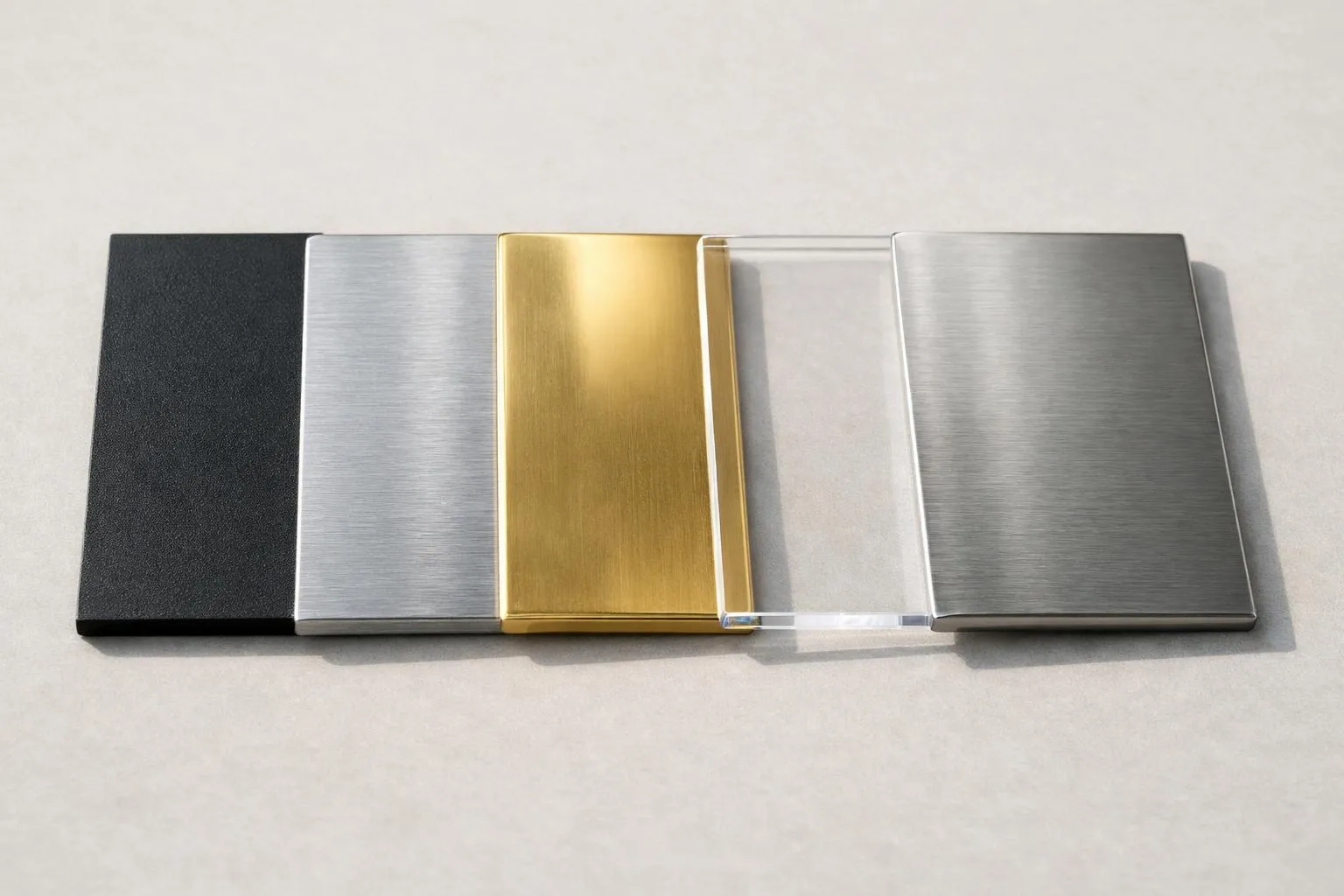 Close-up detailed view of different mailbox nameplate materials displayed side by side on a neutral surface, showing the textures and finishes of PVC, aluminum, brass, plexiglass and stainless steel samples with varying surface treatments and colors, photographed in natural daylight with soft shadows, professional product photography style for a real estate magazine, no text visible