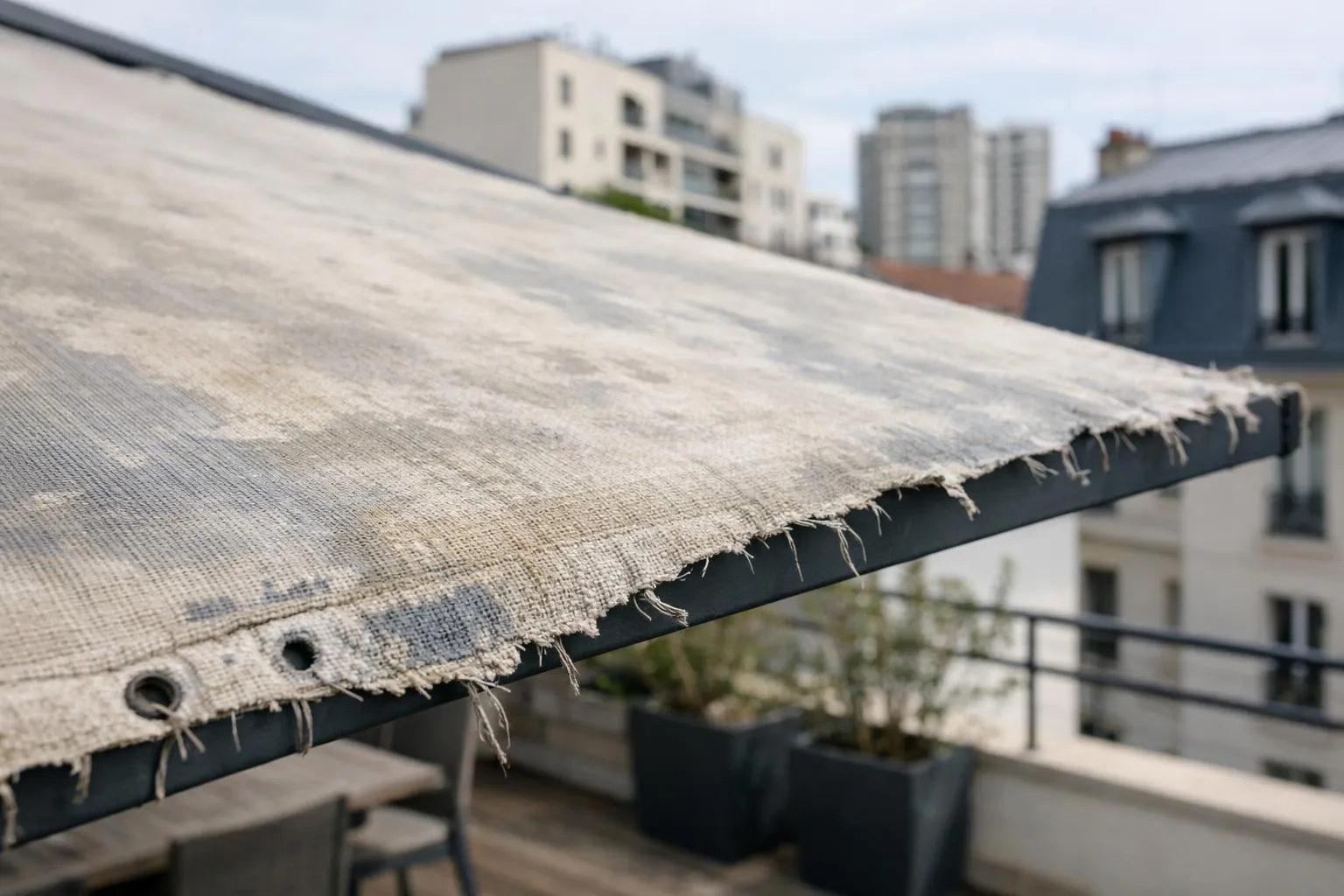 Balcon en toile déchiré avec vue sur les bâtiments urbains.